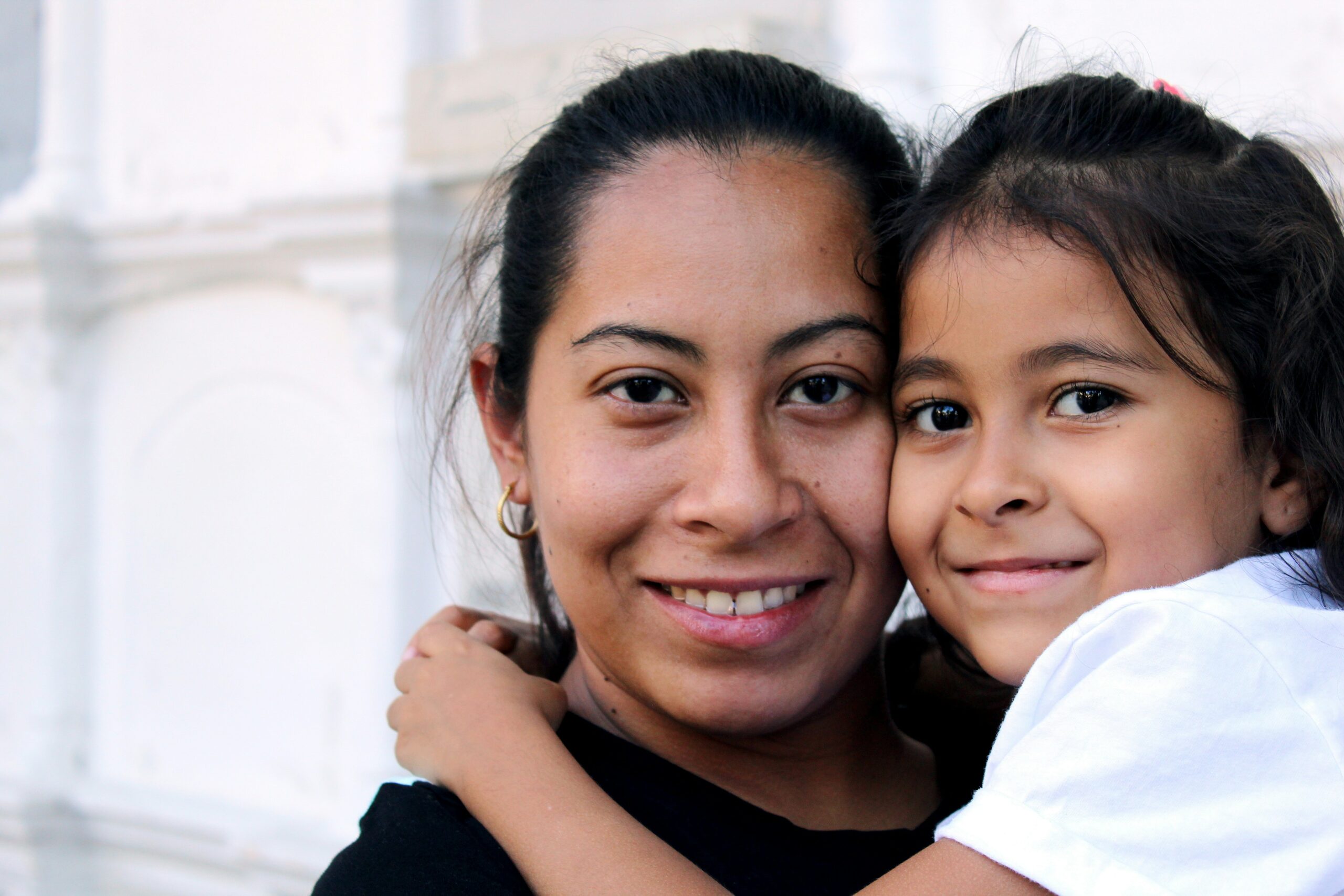 A woman holding her daughter and looking at the camera together.